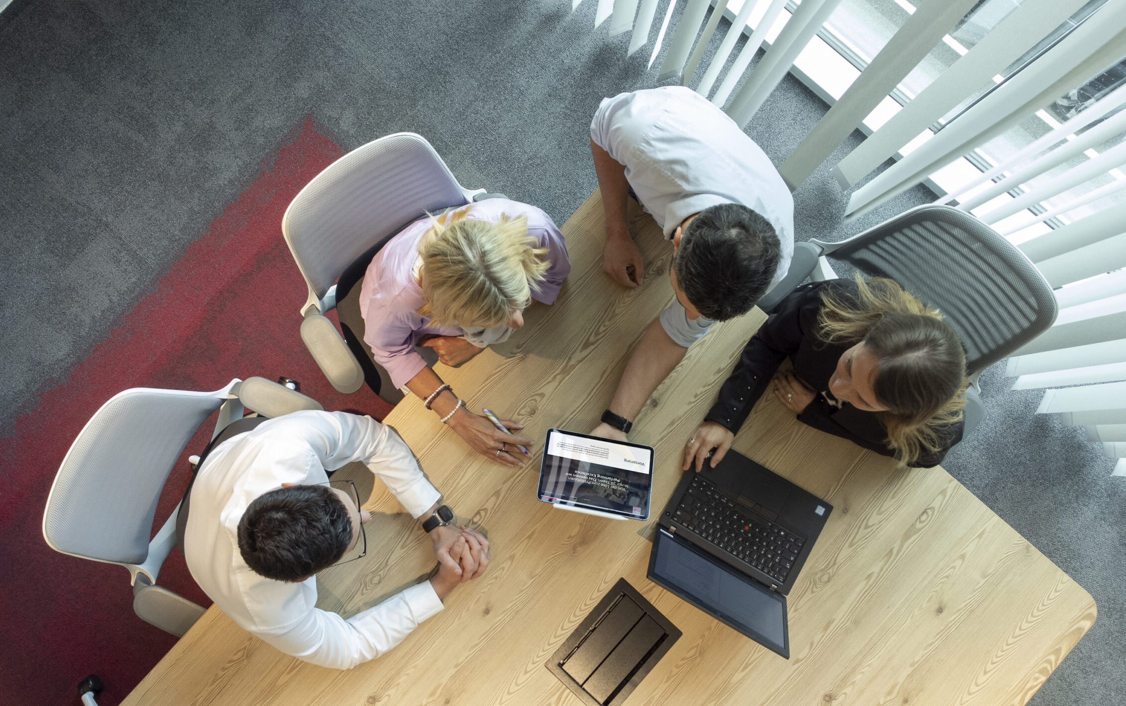 Vier Personen besprechen sich am Tisch mit Laptop und Tablet