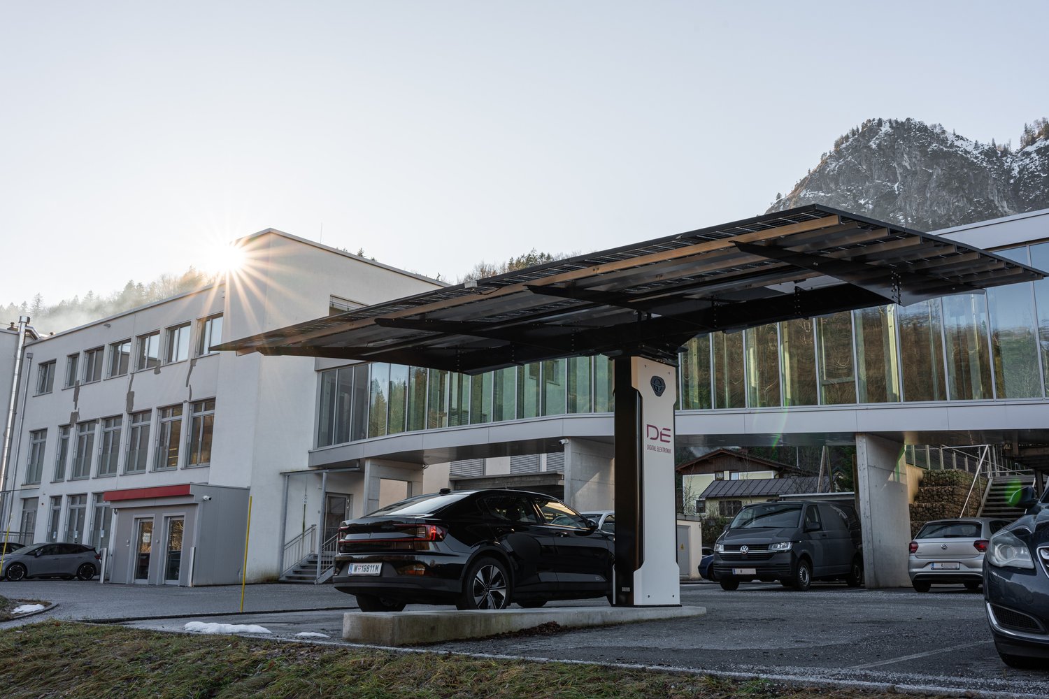 Ladepunkt mit Solardach vor Firmengebäude bei Sonnenaufgang